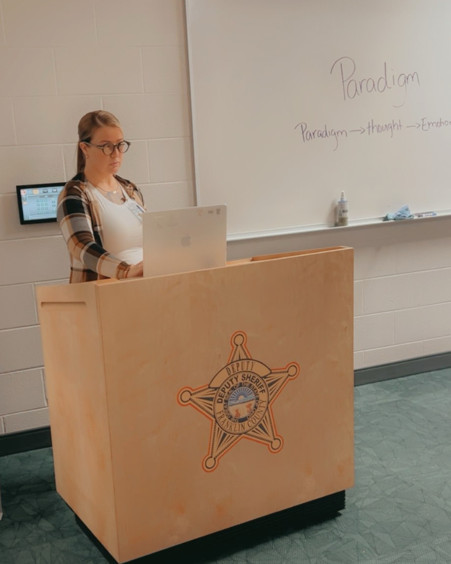 Courtney P. Lacey speaking at a Deputy Sheriff podium inside a correctional facility